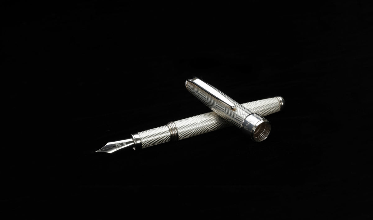 Silver fountain pen with its cap beside it, on a black background