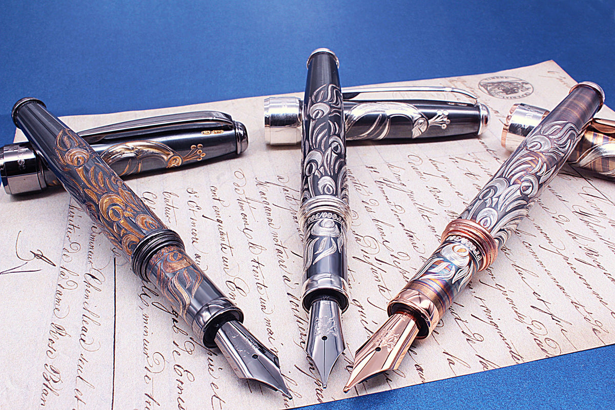 Three silver fountain pens with scroll decorations, resting on an old handwritten letter